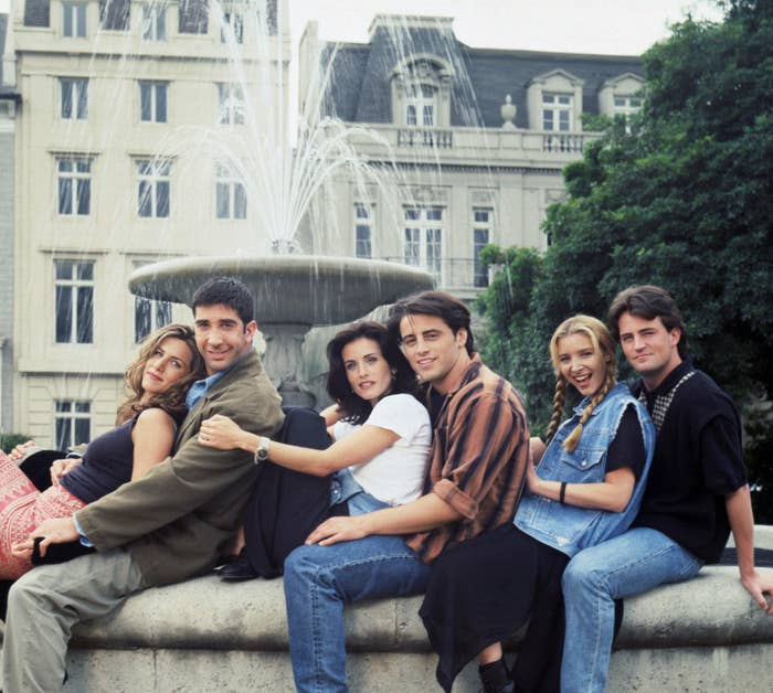 Jennifer Aniston, David Schwimmer, Courteney Cox, Matt LeBlanc, Lisa Kudrow, and Matthew Perry sit closely together on a fountain ledge, posing for a photo