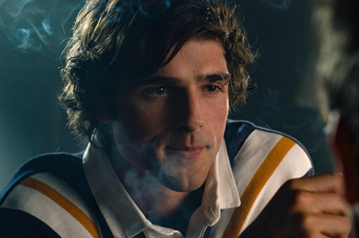 A person wearing a striped shirt is seen in conversation, partially obscured by smoke, in a still from a TV show or movie