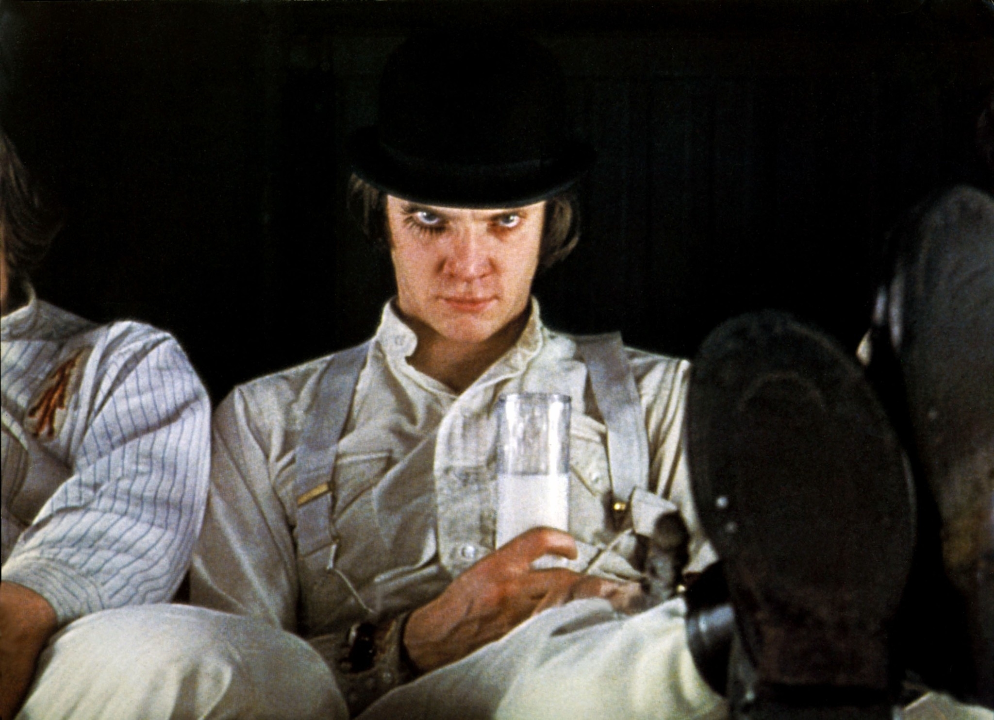 Malcolm McDowell as Alex DeLarge from "A Clockwork Orange," wearing a bowler hat and white outfit, reclining with a glass of milk