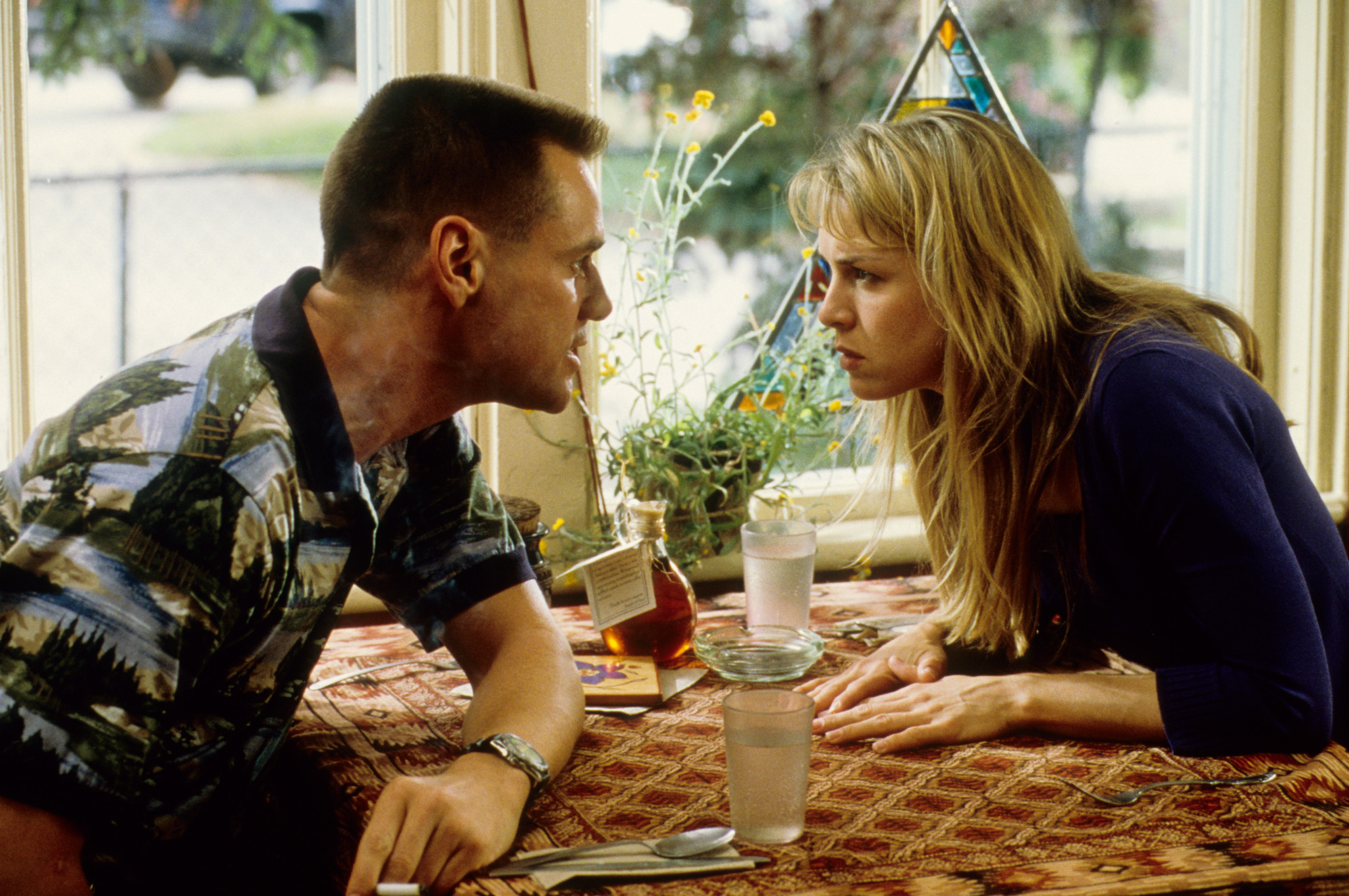 Jim Carrey and Renée Zellweger in an intense scene, facing each other across a table with drinks on it