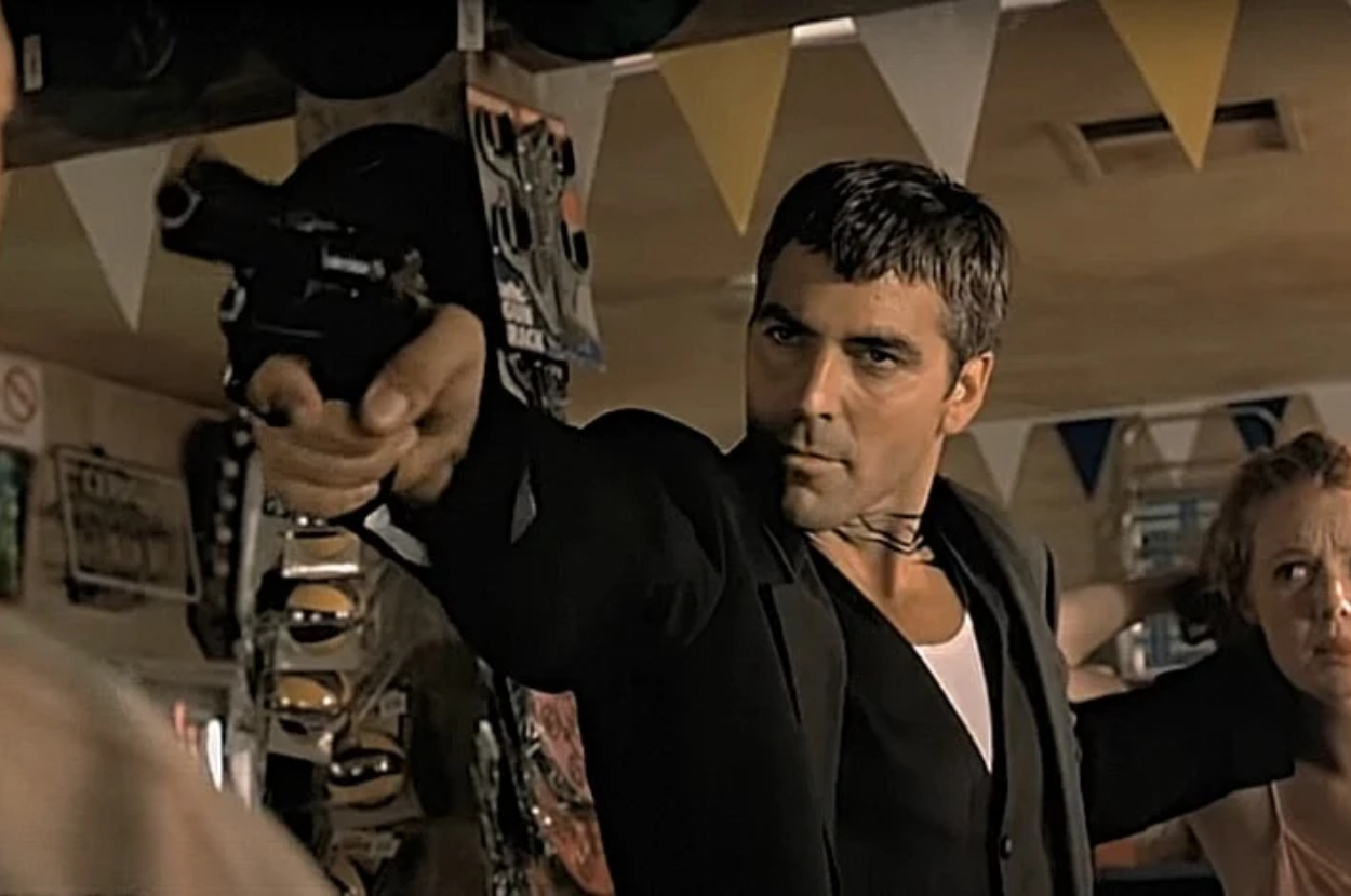 George Clooney pointing a gun while wearing a suit in a scene from the movie "From Dusk Till Dawn."