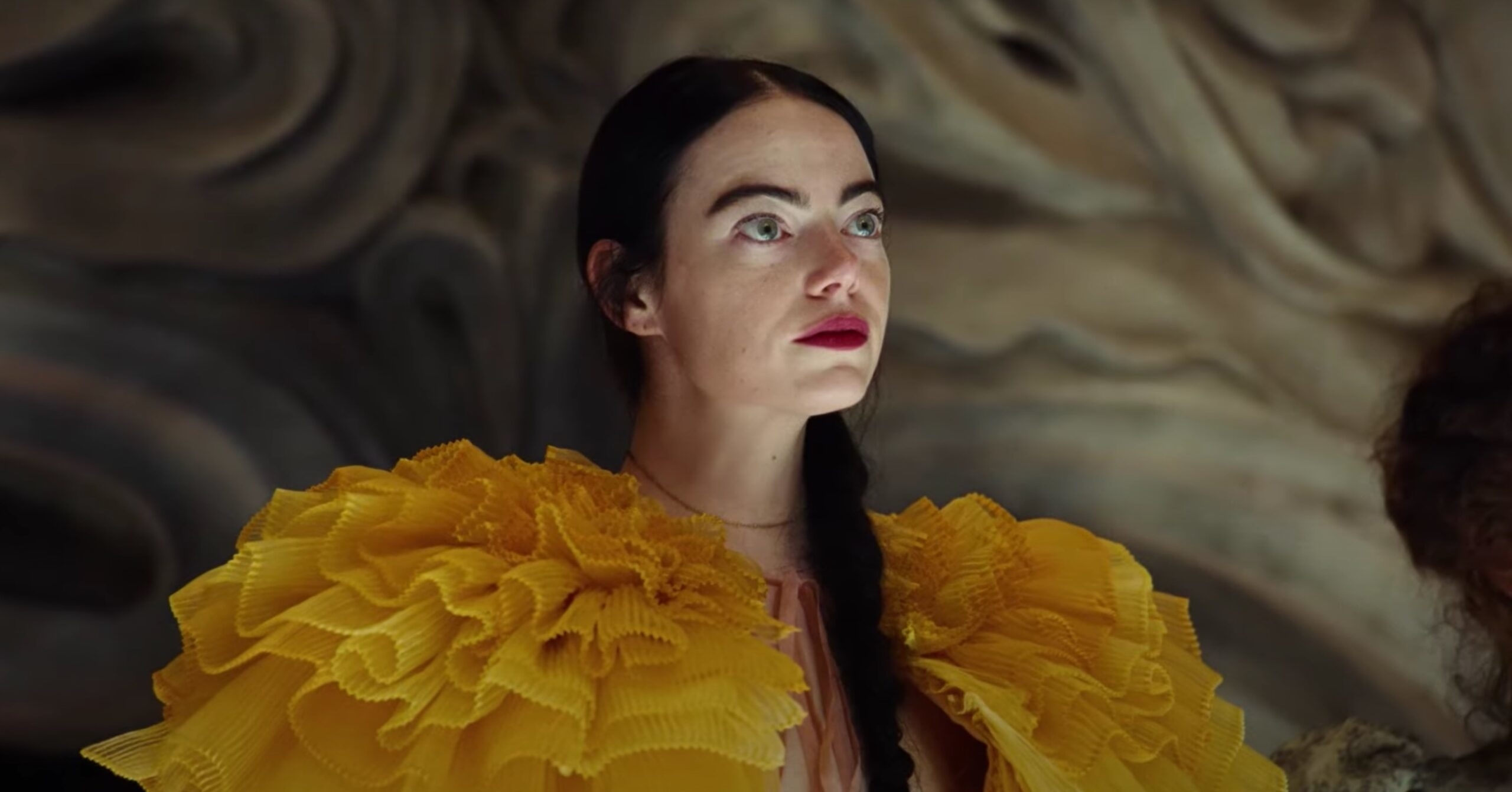 Emma Stone as Cruella de Vil in a dramatic scene from the film "Cruella," wearing an extravagant yellow ruffled garment