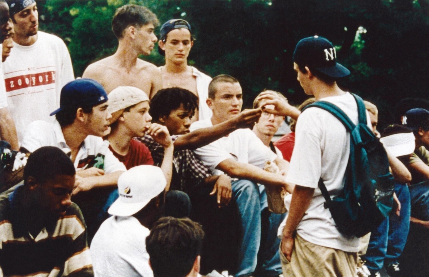 A group of young people, including Justin Pierce and Leo Fitzpatrick, sitting and standing in casual clothing, having a conversation outdoors