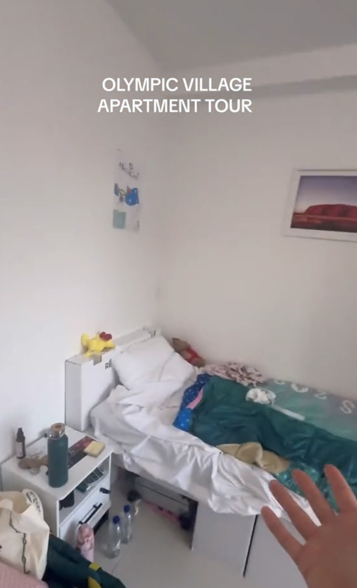 A small, tidy bedroom in the Olympic Village with an unmade bed, decorations on the walls, and the text "Olympic Village Apartment Tour."