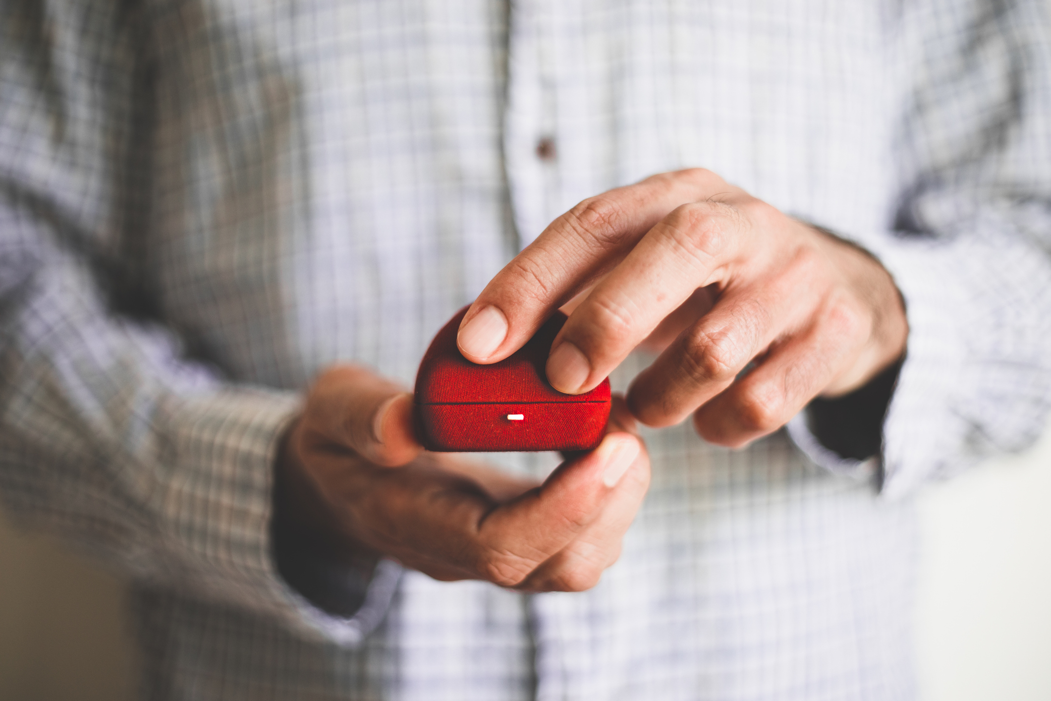 A person in a plaid shirt holds a red ring box, suggesting a proposal or engagement