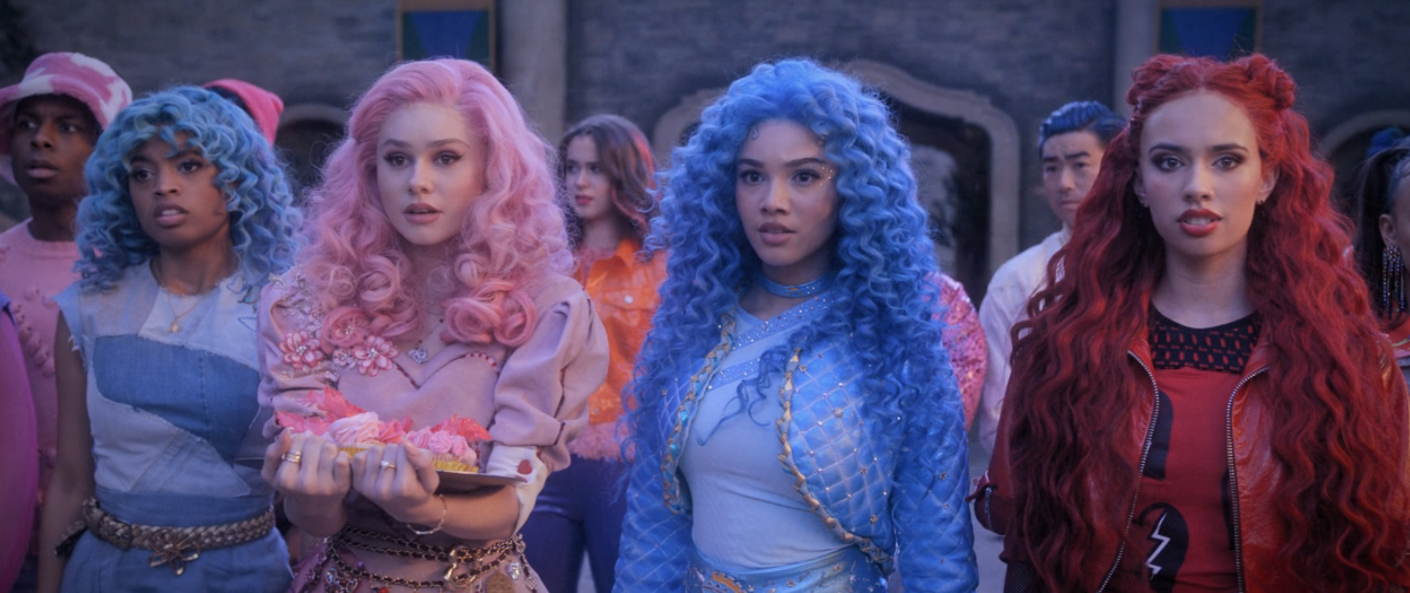 Ella, Bridget, Chloe, and Red standing together, wearing stylized outfits with striking hair styles in bold colors. Bridget is holding cupcakes.