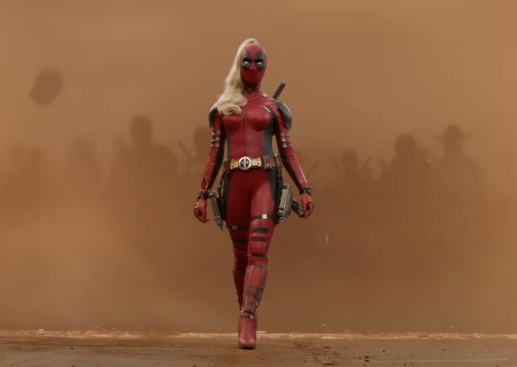 Lady Deadpool, in a red and black suit, strides confidently amid a sandstorm