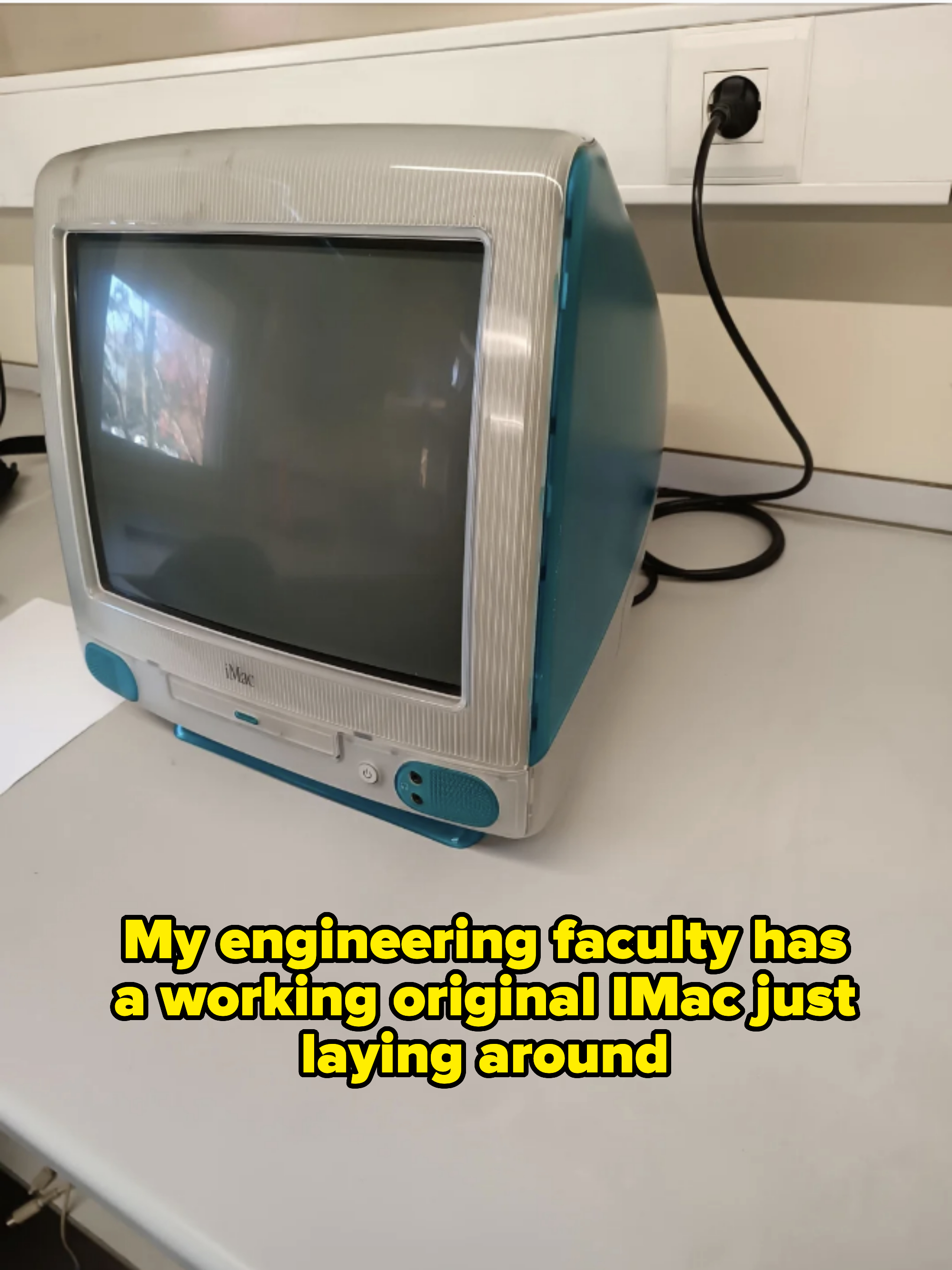 A vintage Apple iMac G3 computer on a grey desk with a white power outlet in the background