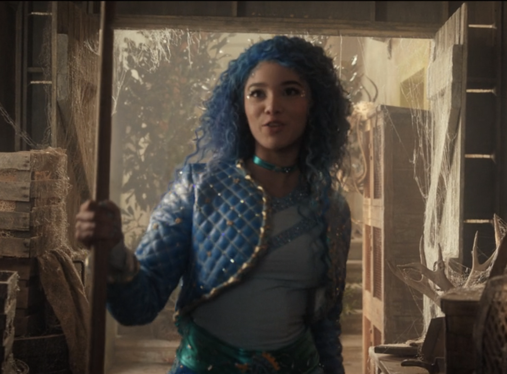 Chloe holds a broom, singing in a cluttered room