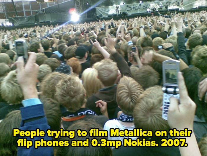 A large crowd at a concert, with many attendees holding up cell phones to capture the performance on stage. The image captures the energy of the live event