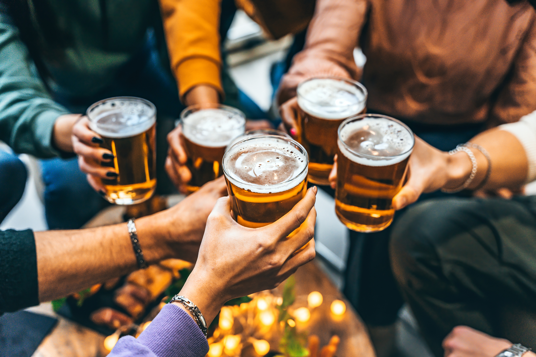 A group of people clinks glasses of beer together at a casual gathering with food on a table