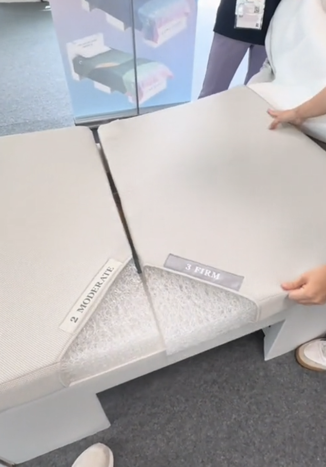Two firm and moderate mattresses are flipped open to show interior materials. Two hands, part of the image, hold the mattresses