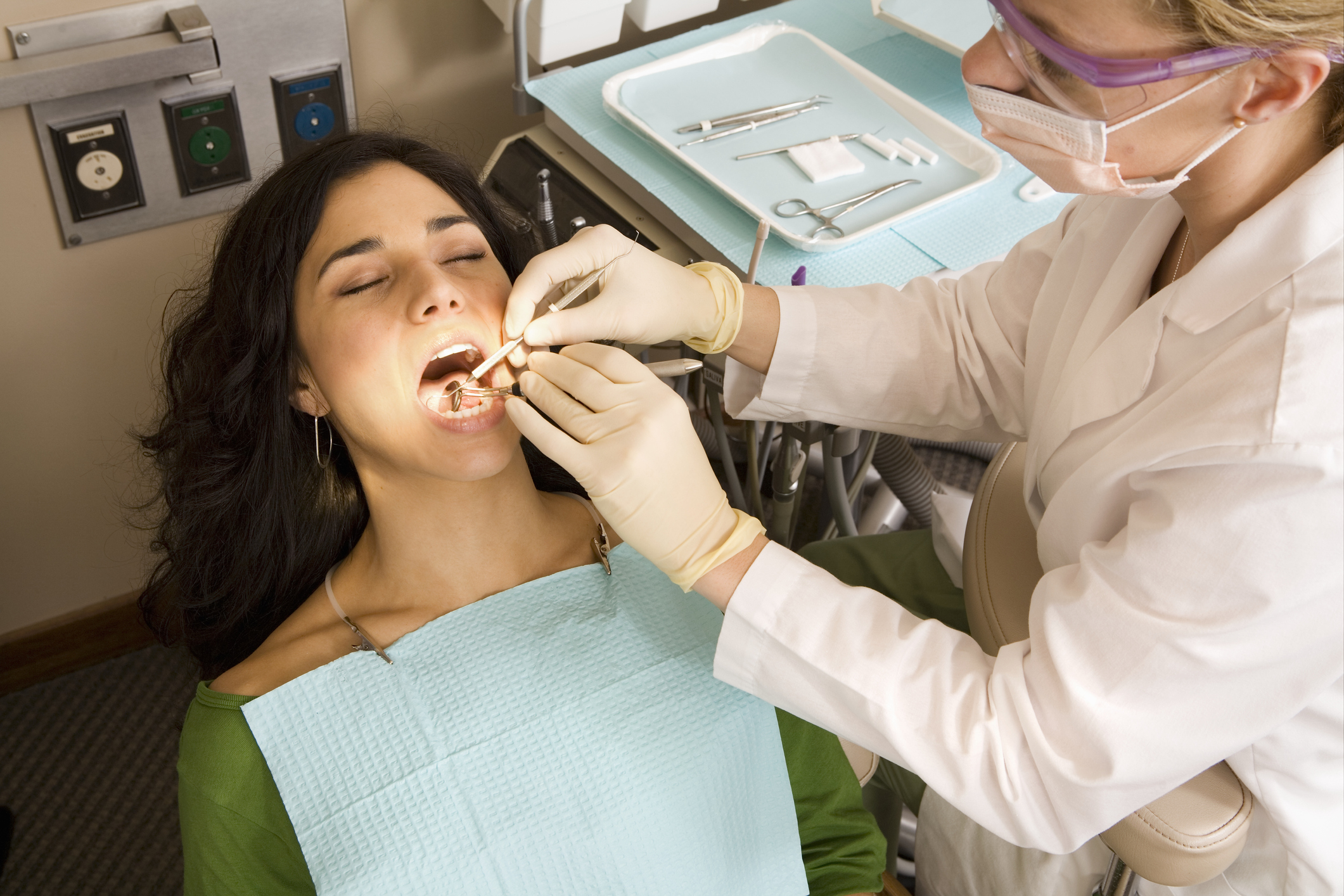 Patient receiving a dental exam from a dentist. Dental tools and equipment are visible in the background. No celebrity present