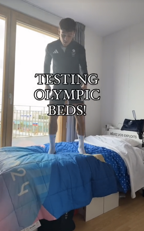 An athlete, testing the sturdiness of an Olympic bed, stands on it with text reading "TESTING OLYMPIC BEDS!"
