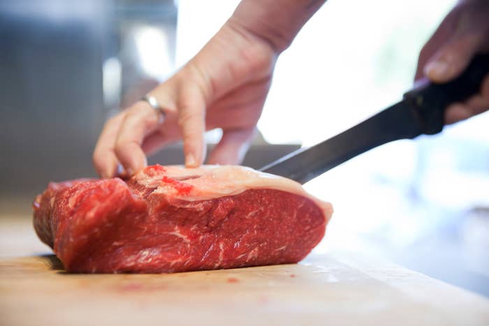 A hand is carving a raw cut of meat with a knife on a cutting board