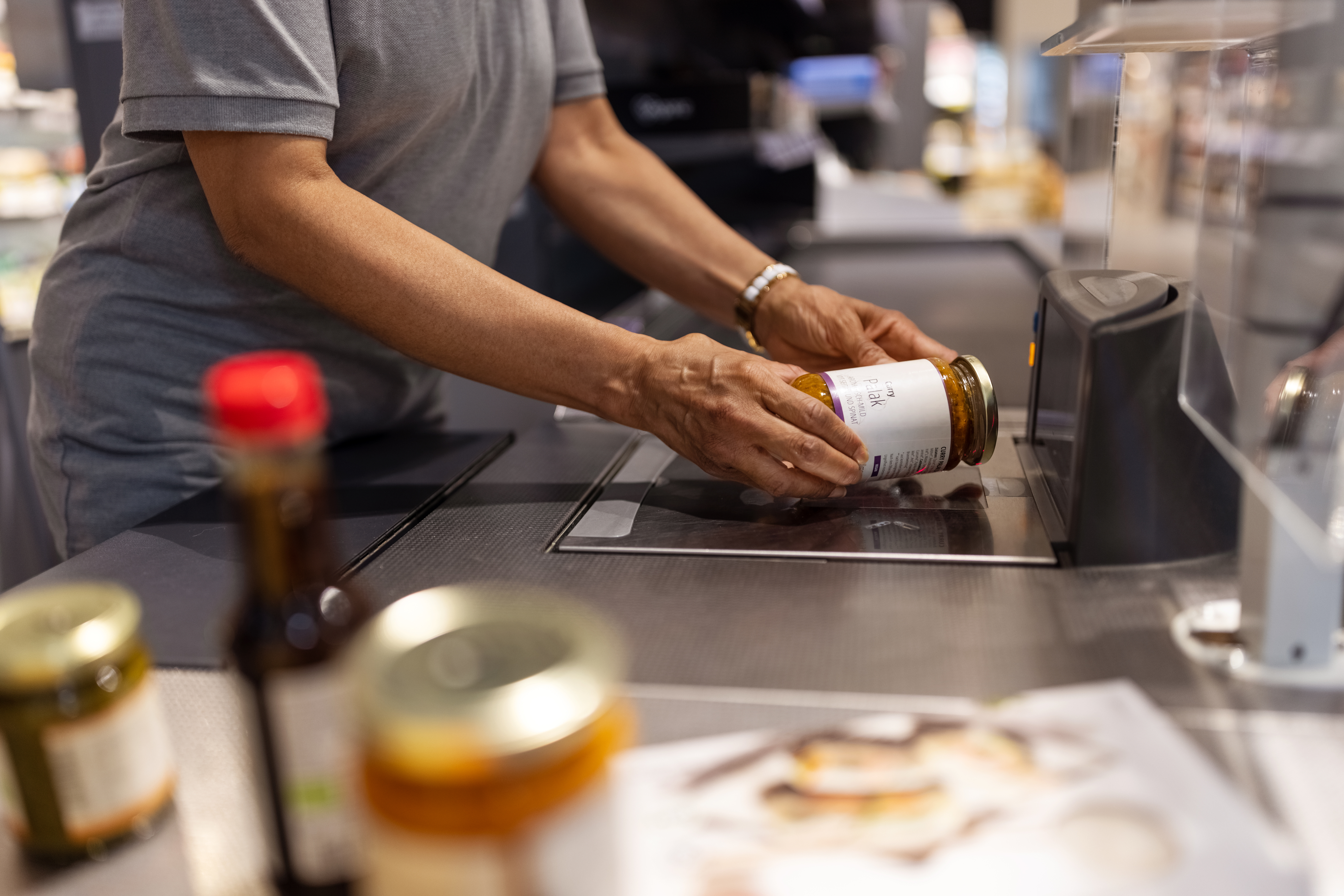 A person scans a jar of sauce at a self-checkout in a grocery store