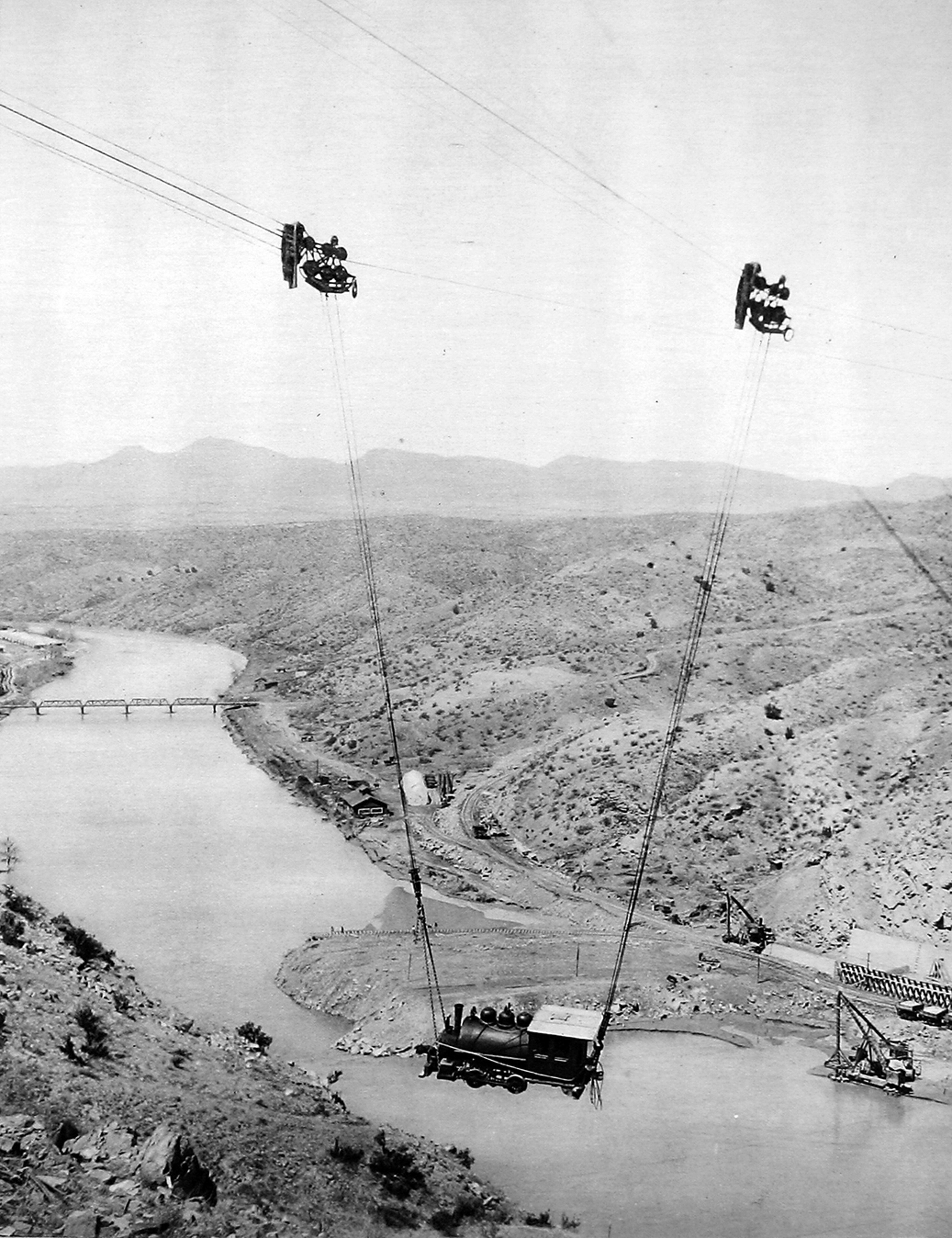 Historical photograph of construction workers suspended by cables across a river gorge during the building of the Roosevelt Dam in Arizona, early 20th century