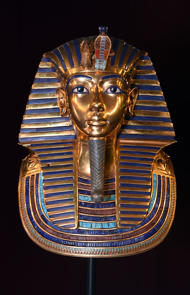 Egyptian pharaoh Tutankhamun's golden burial mask adorned with intricate designs and semi-precious stones, displayed against a dark background