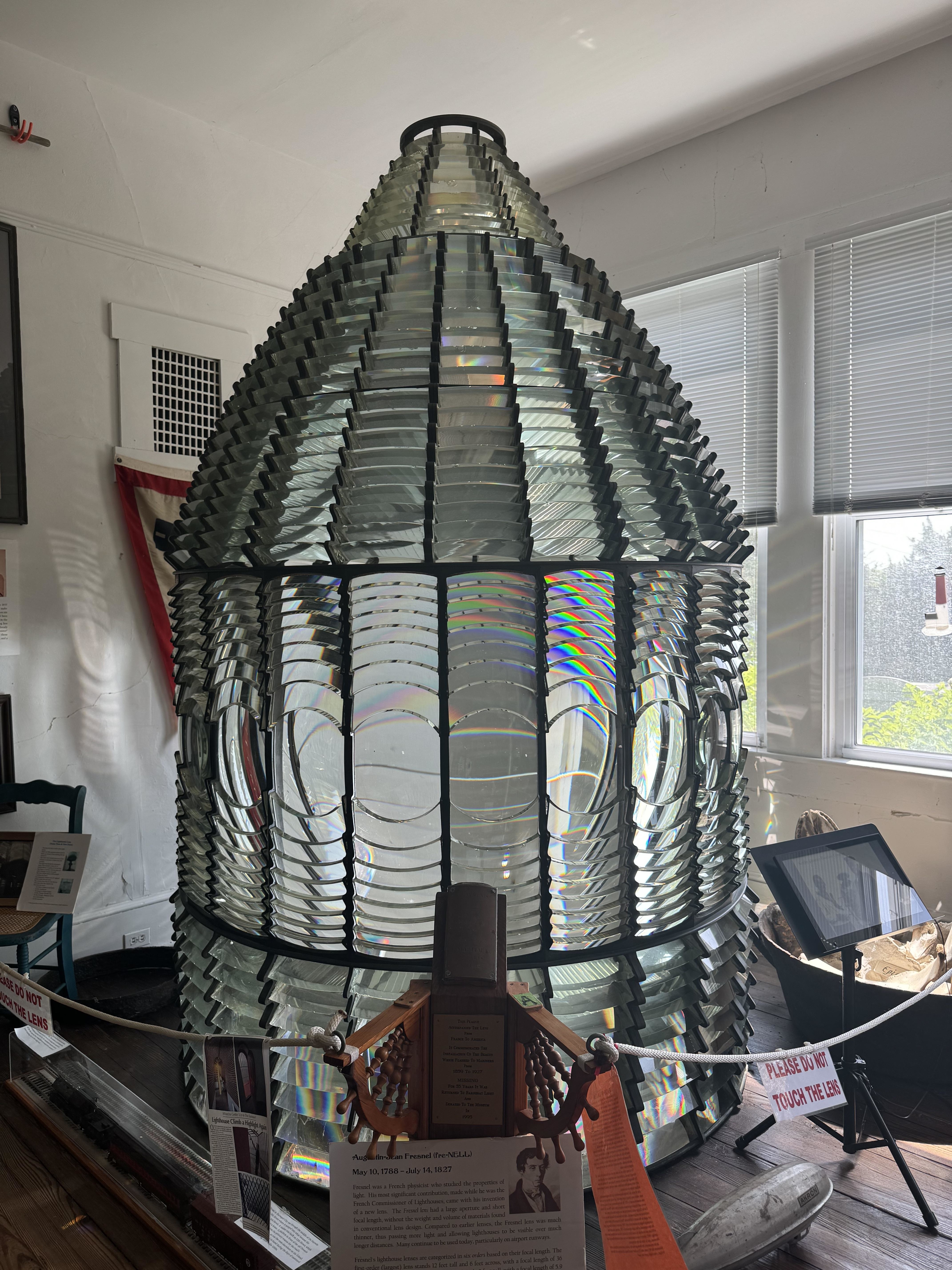 A large Fresnel lens display in a museum with informational plaques and signs around it