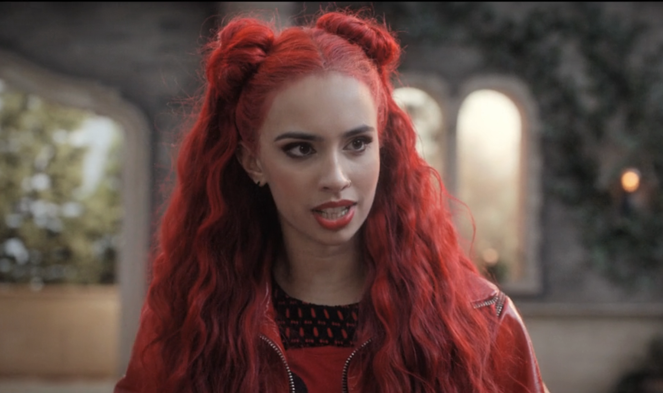 Kylie as Red with long hair with space buns, leather jacket, and bold lipstick