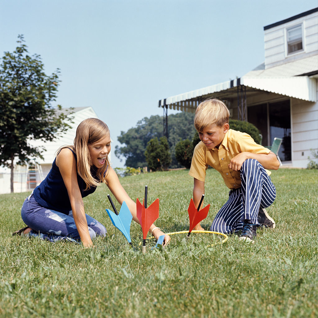 Two children are playing lawn darts together outside on a grassy lawn