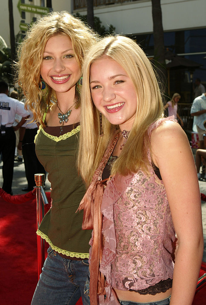 Vanessa Lengies and AJ Michalka smile on the red carpet, wearing casual tops with intricate patterns and necklaces