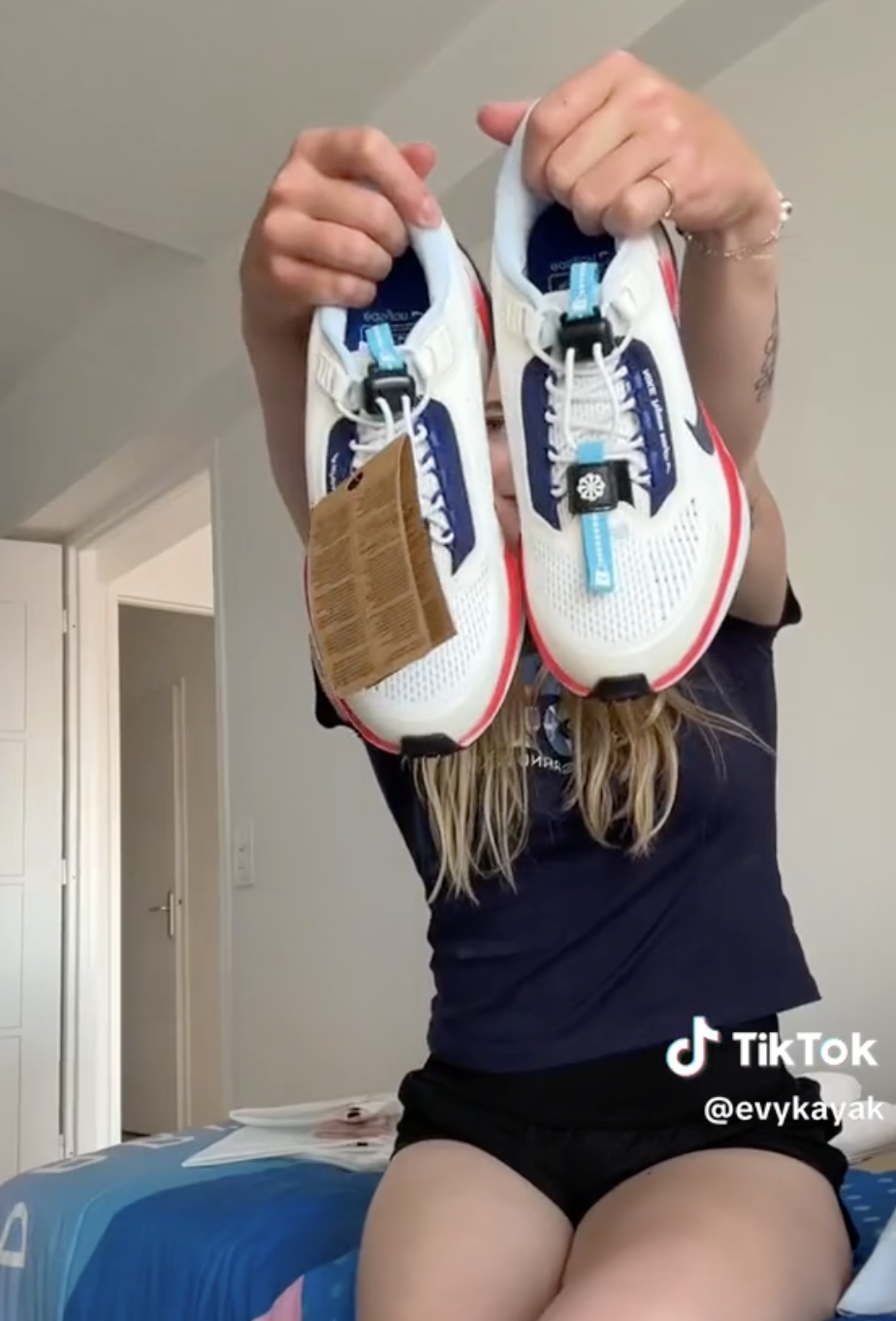 A person presenting a pair of athletic shoes, holding them up to the camera. The image is watermarked with the TikTok handle &quot;@evykayak.&quot;