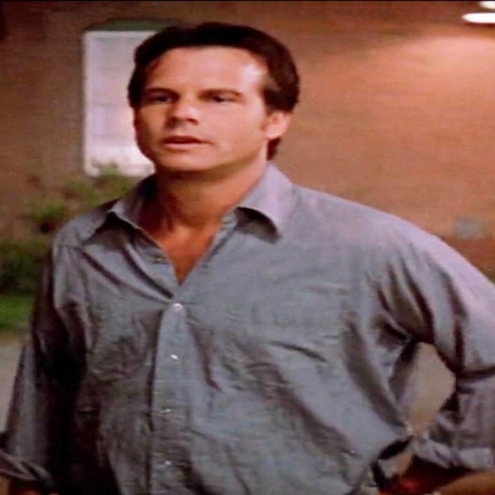 A man stands with his hands behind his back, wearing a casual button-down shirt. The background features an outdoor evening scene