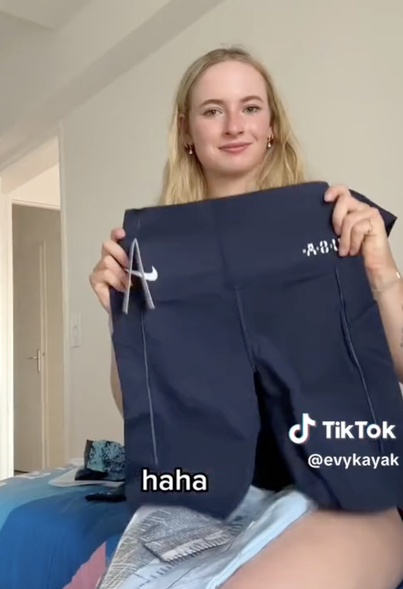 A woman, likely @evykayak from TikTok, smiles and holds up a pair of Nike shorts in a room. Text in the image reads &quot;haha.&quot;