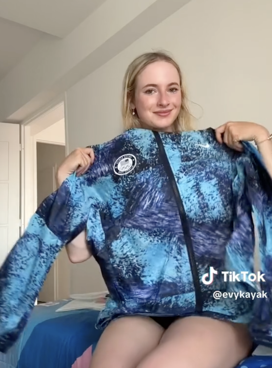 Woman with long hair, smiling and holding up a blue jacket. TikTok handle &quot;@evykayak&quot; is visible in the bottom right corner