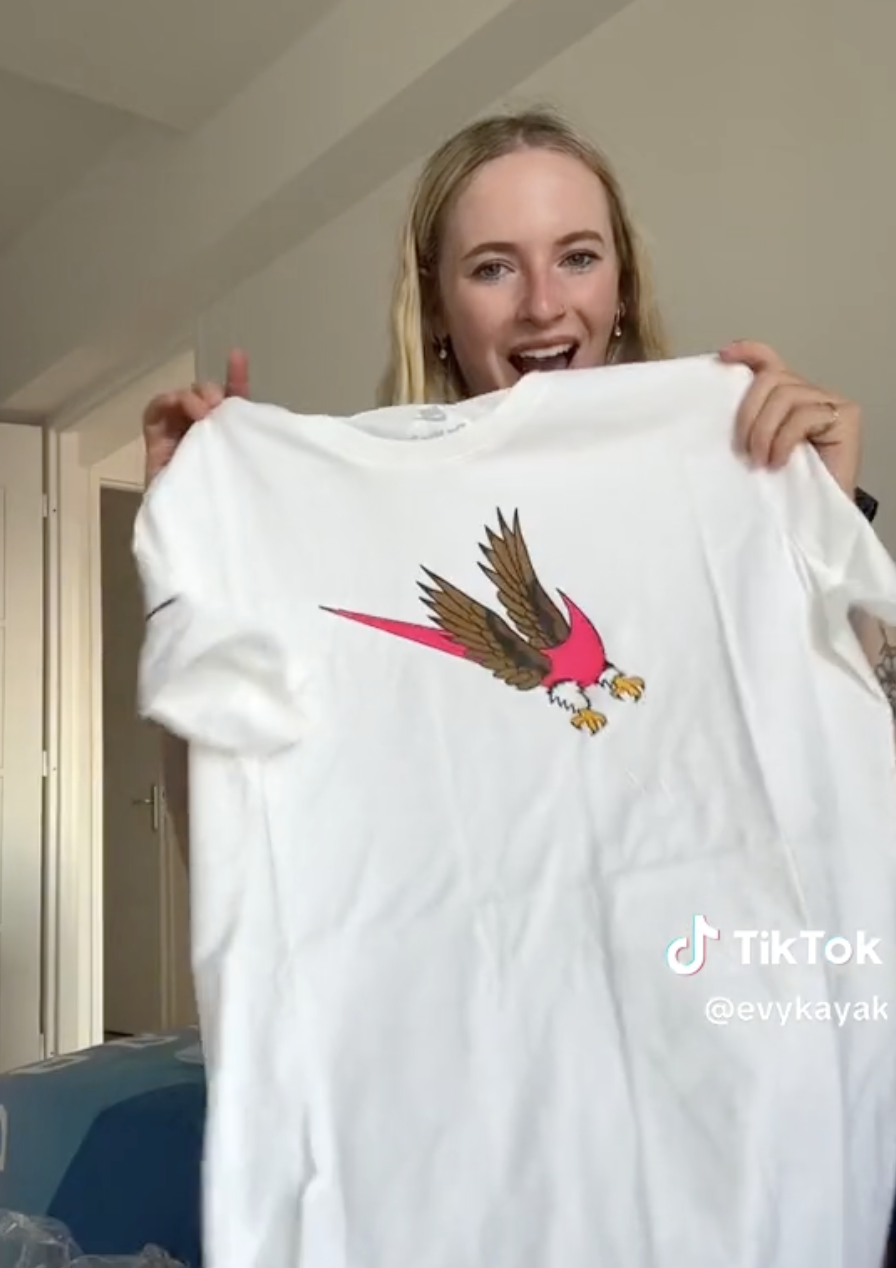 Person holding up a white t-shirt with a bird graphic. TikTok handle @evykayak is visible