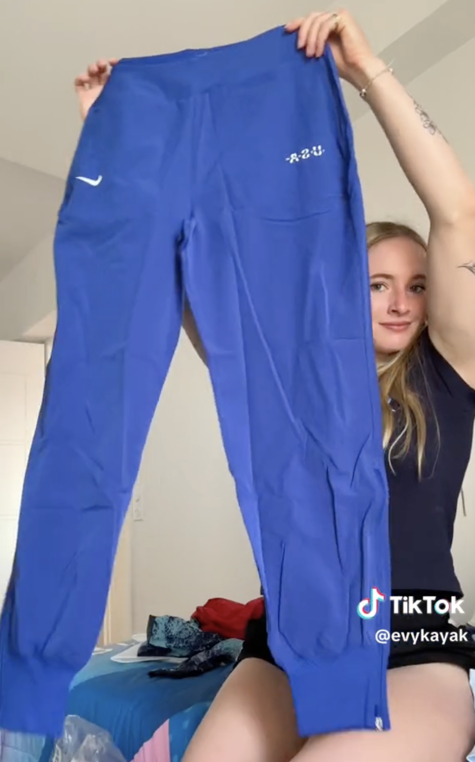 Evy Leibfarth holds up blue athletic pants, sharing a TikTok video from her account @evykayak