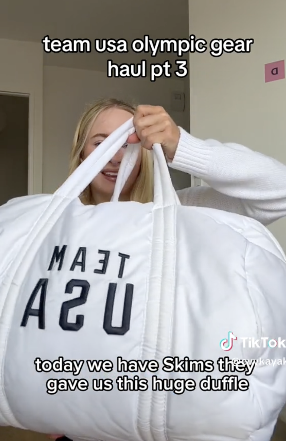 Kayla DiCello holding a large white duffle bag with &quot;Team USA&quot; text. Caption reads: &quot;team usa olympic gear haul pt 3. Today we have Skims they gave us this huge duffle&quot;