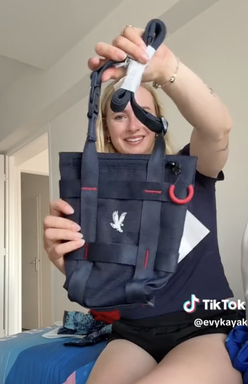 Person holding a small bag in front of the camera with a smiling expression. TikTok username @evykayak is watermarked in the bottom right corner