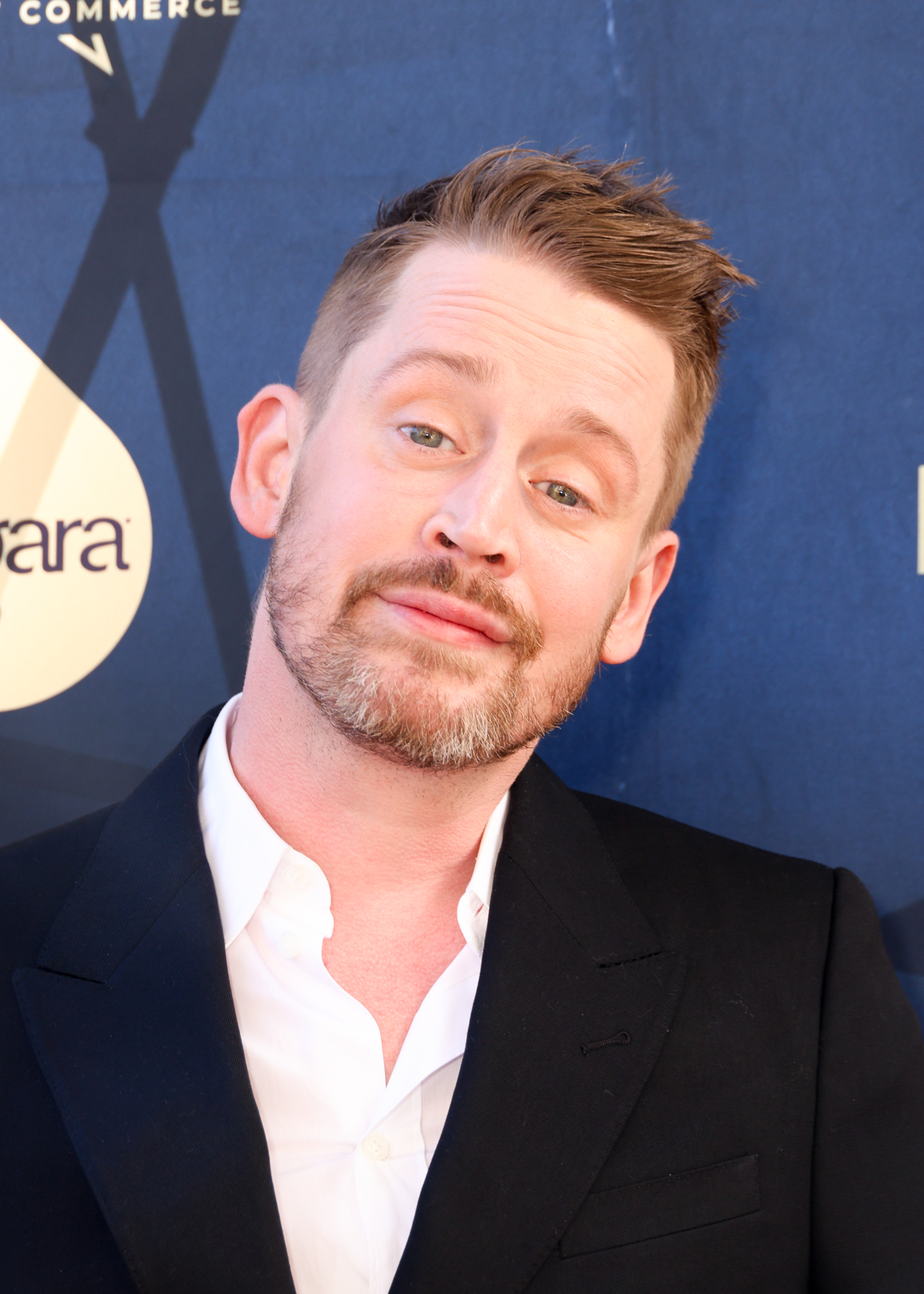 Macaulay Culkin poses on the red carpet, wearing a white shirt and black blazer