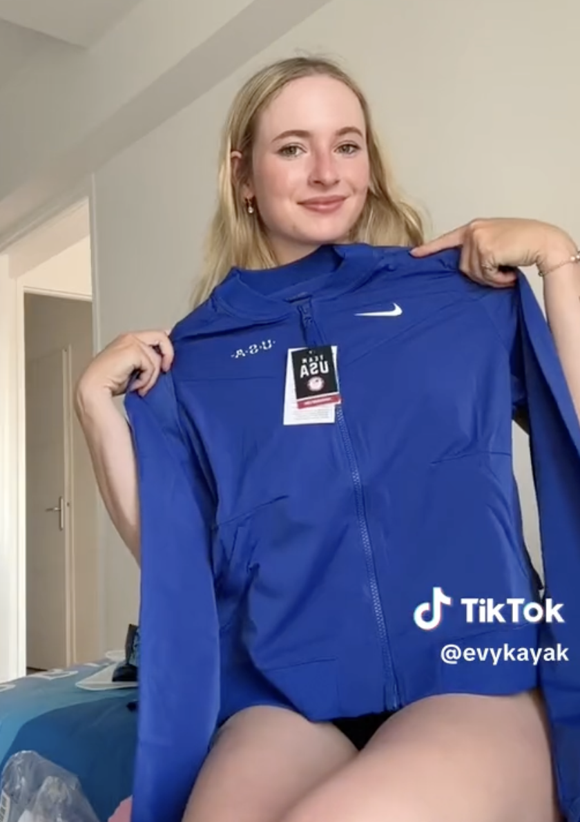 Person holding a blue Nike jacket with a tag, smiling at the camera, username @evykayak displayed on the right side of the image