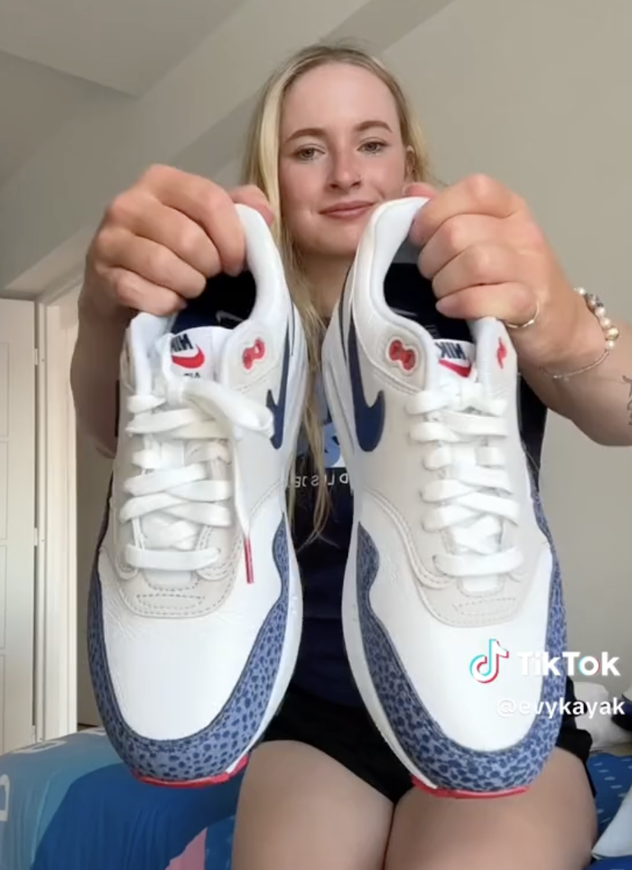 Person in a casual outfit holding a pair of Nike Air Max sneakers toward the camera