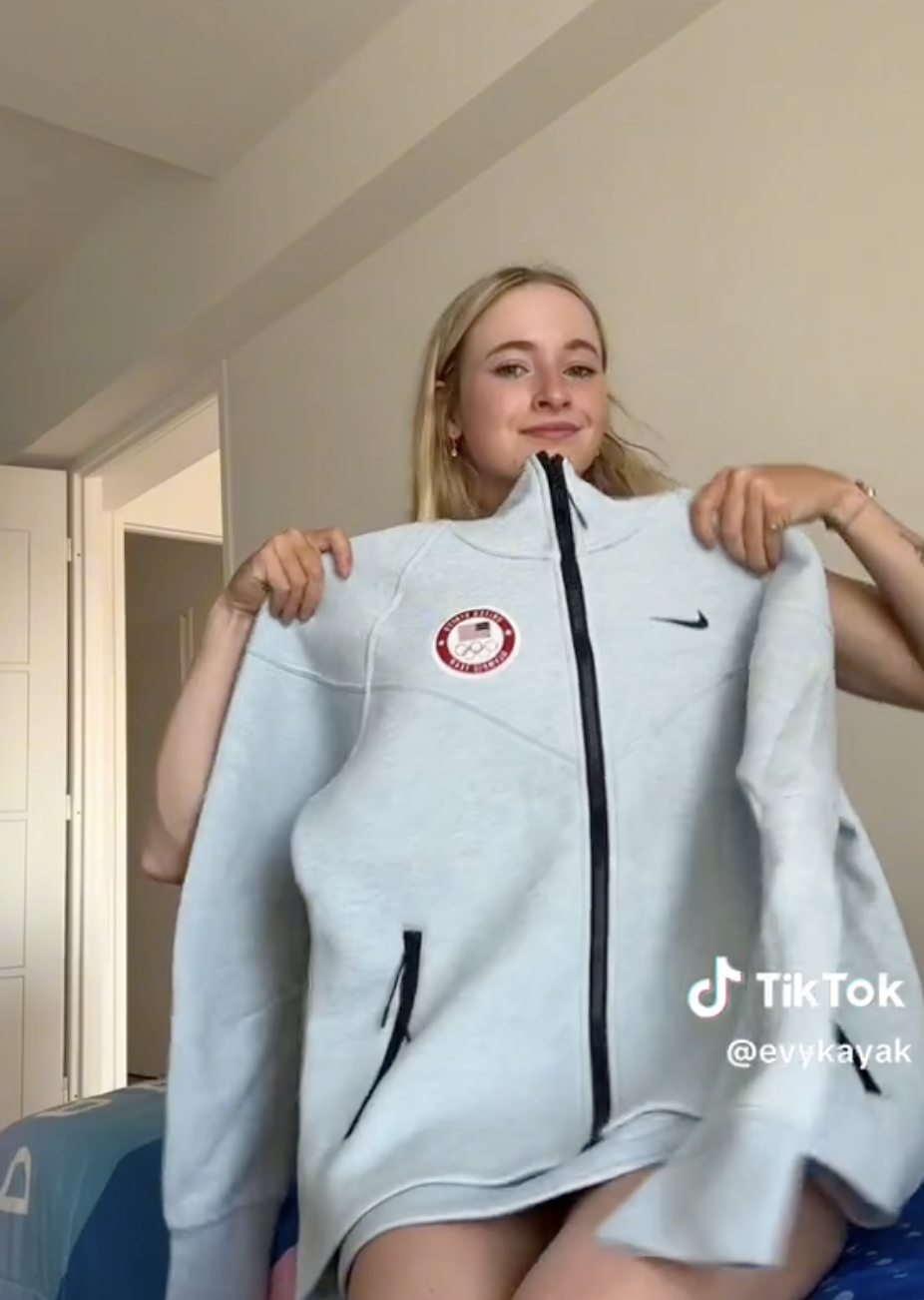 Evy Leibfarth holds a gray Team USA jacket in a TikTok video. She appears to be smiling and showing off the jacket's details