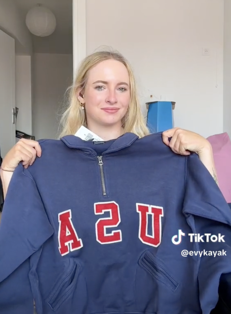 Evykayak poses indoors holding a blue USA sweatshirt in a TikTok video