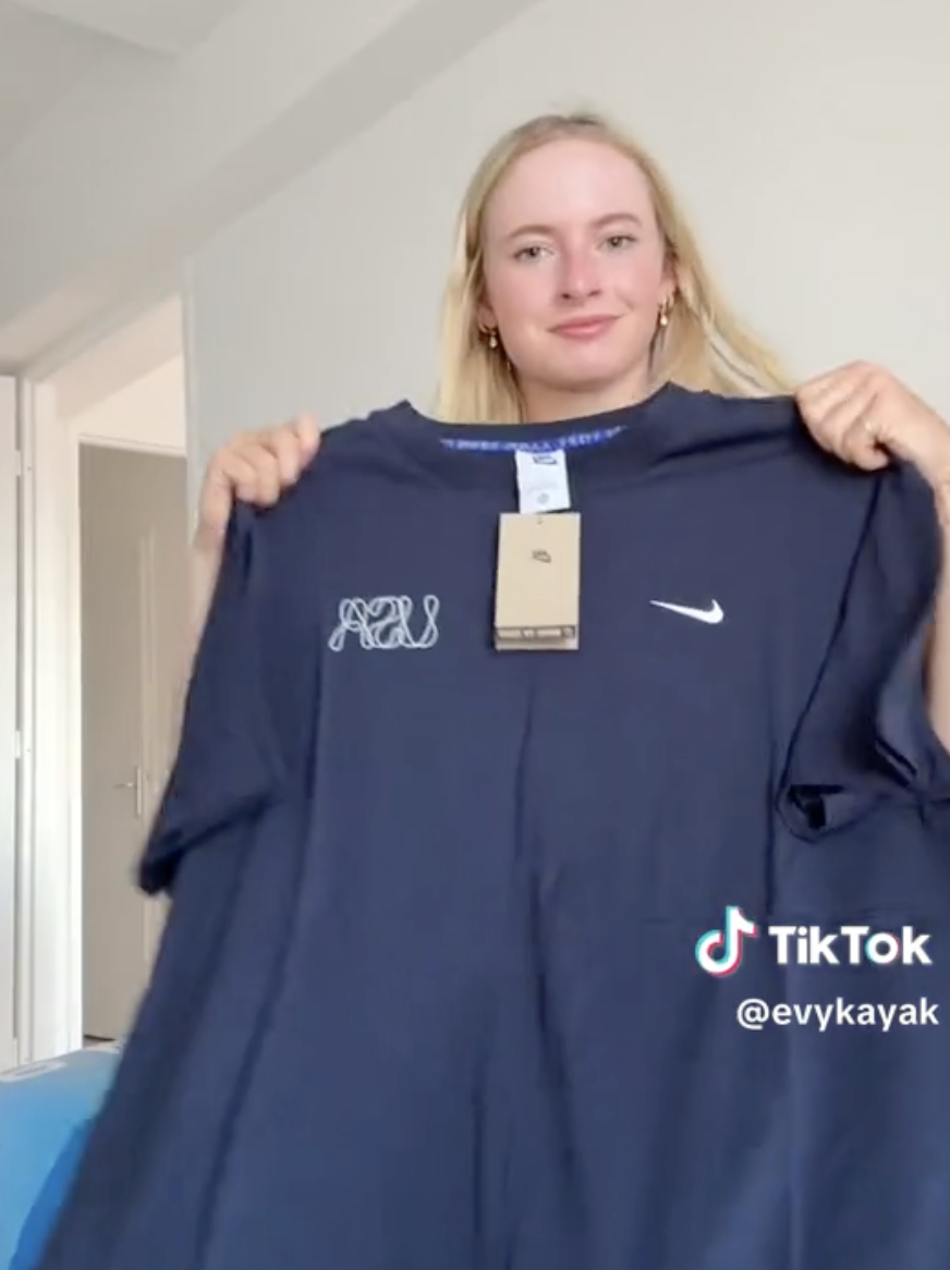 Evy Kayak holds up a large Nike t-shirt with a smile, in a TikTok video
