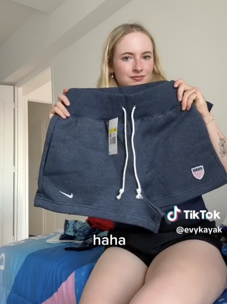 TikTok user @evykayak shows a pair of sports shorts while sitting on a bed. The screen displays the text &quot;haha.&quot;
