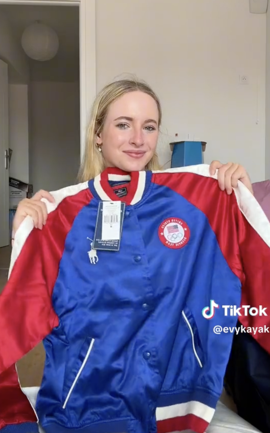 Evykayak holds up a blue and red varsity jacket with a USA insignia, tagging her TikTok handle @evykayak