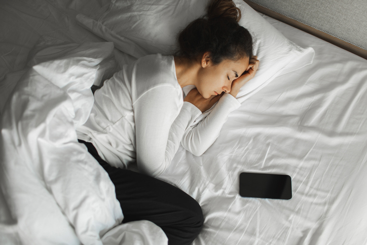 Woman sleeps in bed with a cellphone lying next to her pillow