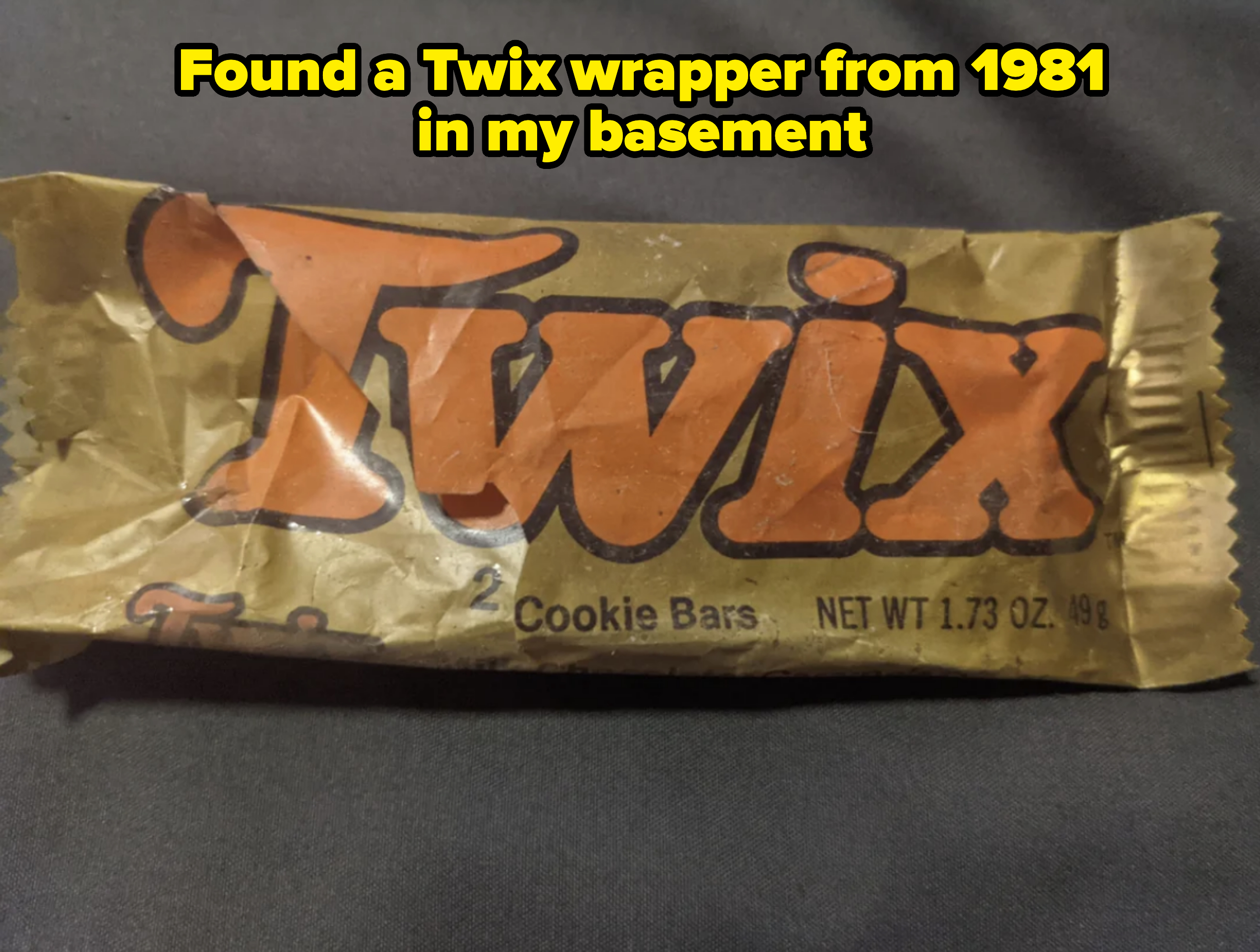 A Twix candy bar in its wrapper which reads "Twix, 2 Cookie Bars, NET WT 1.73 OZ (49g)."