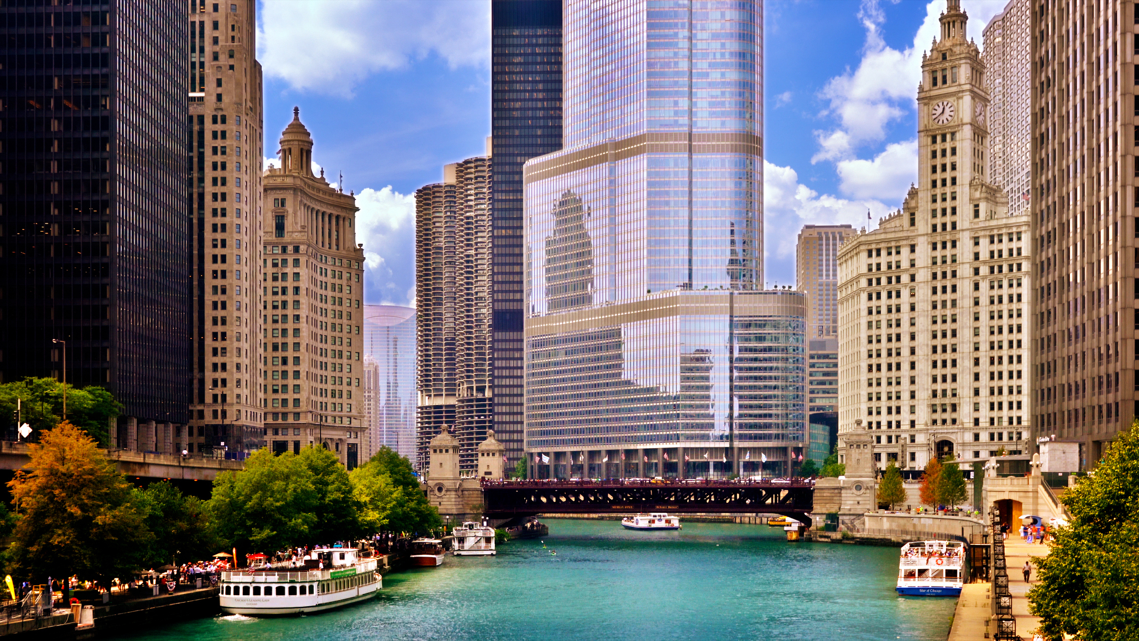 Chicago River in downtown Chicago, with boats on the water and high-rise buildings, including the Trump International Hotel and Tower, lining the riverbanks