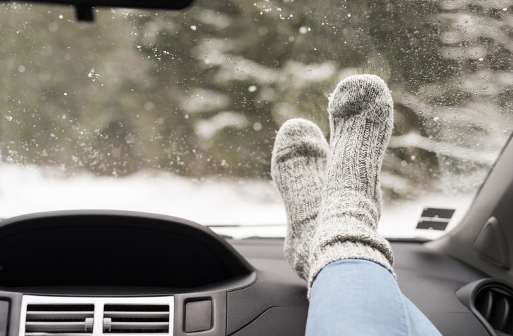 Feet in cozy socks resting on a car dashboard, with a snowy outdoor scene visible through the windshield