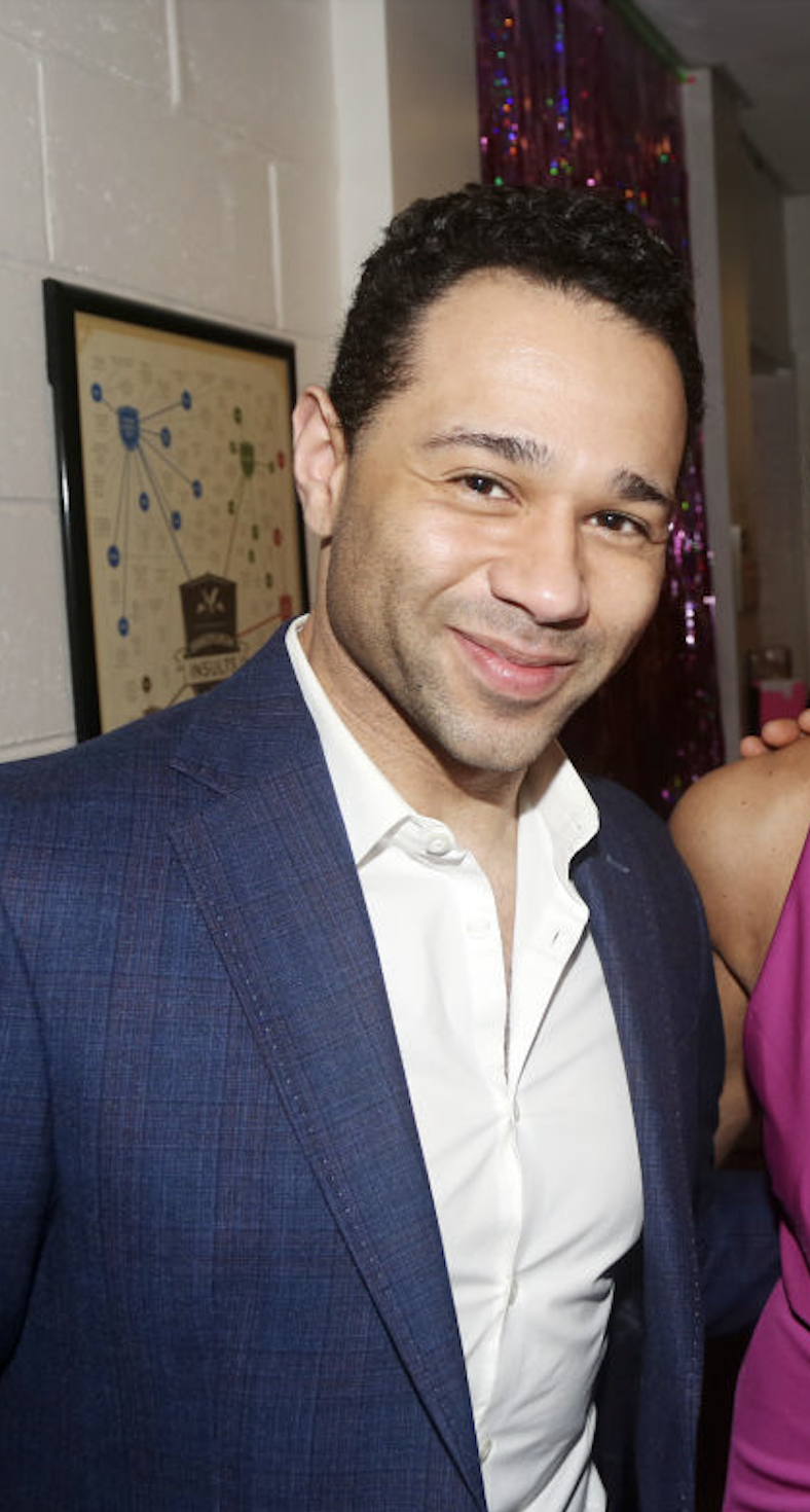 Corbin Bleu smiling, wearing a suit jacket over a white dress shirt at a public event