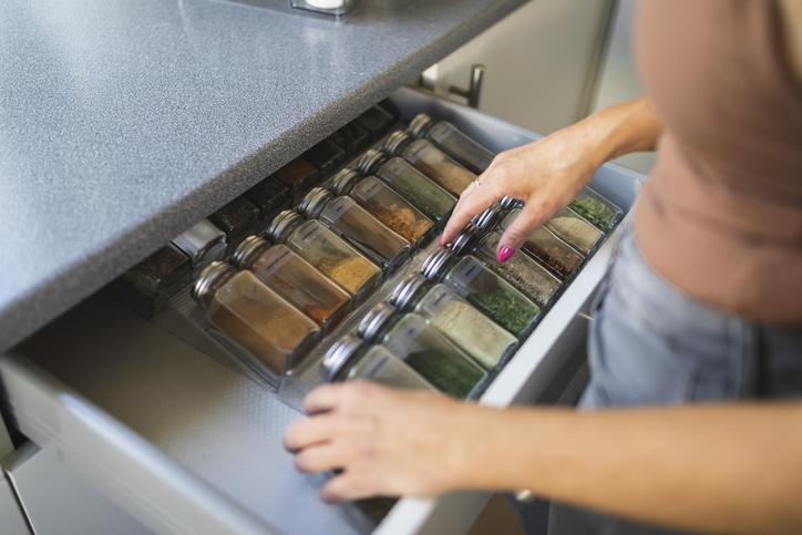 A person organizes a drawer filled with various spices in labeled glass jars