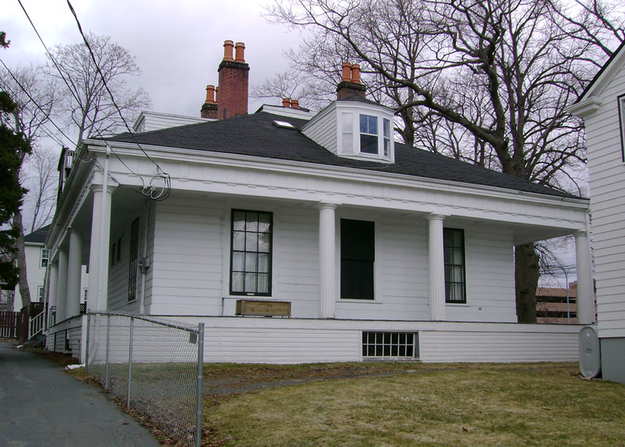 A two-story white house with four tall chimneys, large front columns, and a small attic window. There is one window that is completely blacked out.