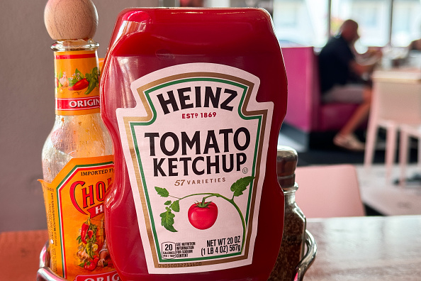 Heinz Tomato Ketchup bottle and Cholula Hot Sauce bottle on a restaurant table, with blurred people seated in the background